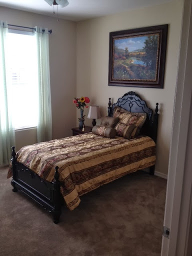 A cozy and well-decorated bedroom featuring a bed with a patterned comforter, floral arrangement, and natural light from the window.