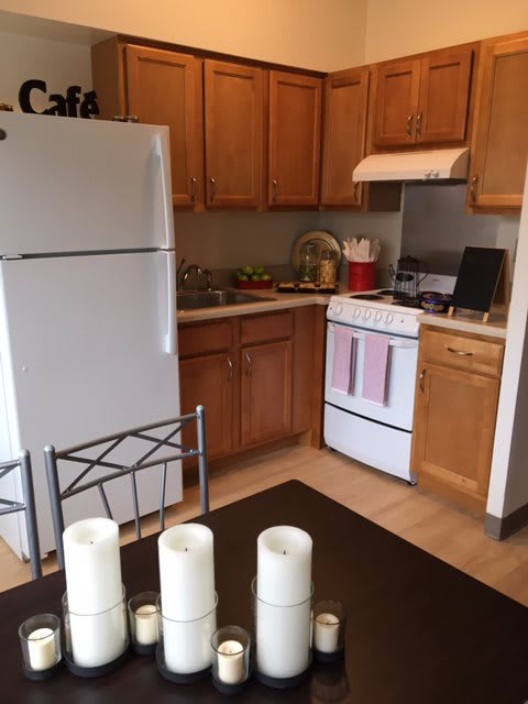 A cozy kitchen with wooden cabinets, featuring a refrigerator and stove, next to a dining table adorned with candles.
