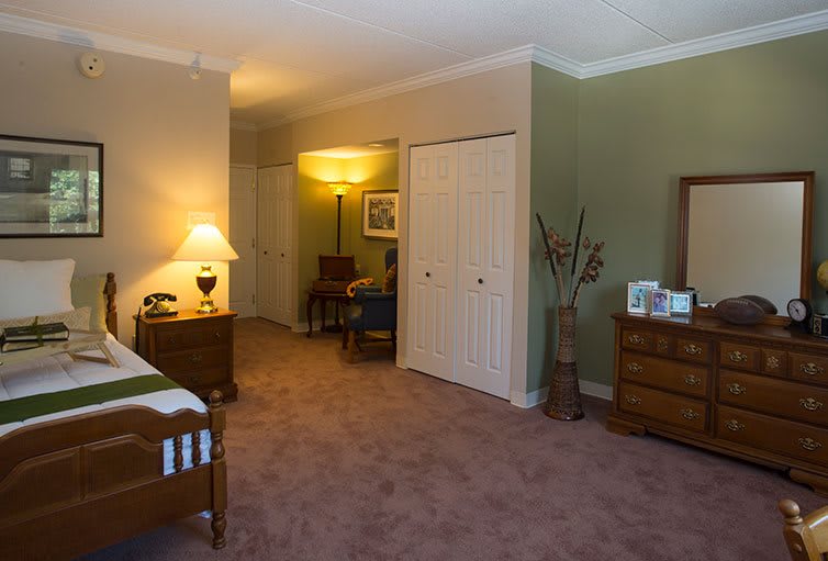 A cozy bedroom with soft lighting, featuring a bed, dresser, and a standing lamp.