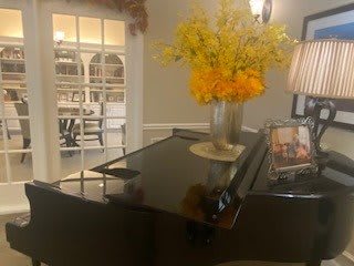 A cozy room with a grand piano adorned with a vase of vibrant yellow and orange flowers.