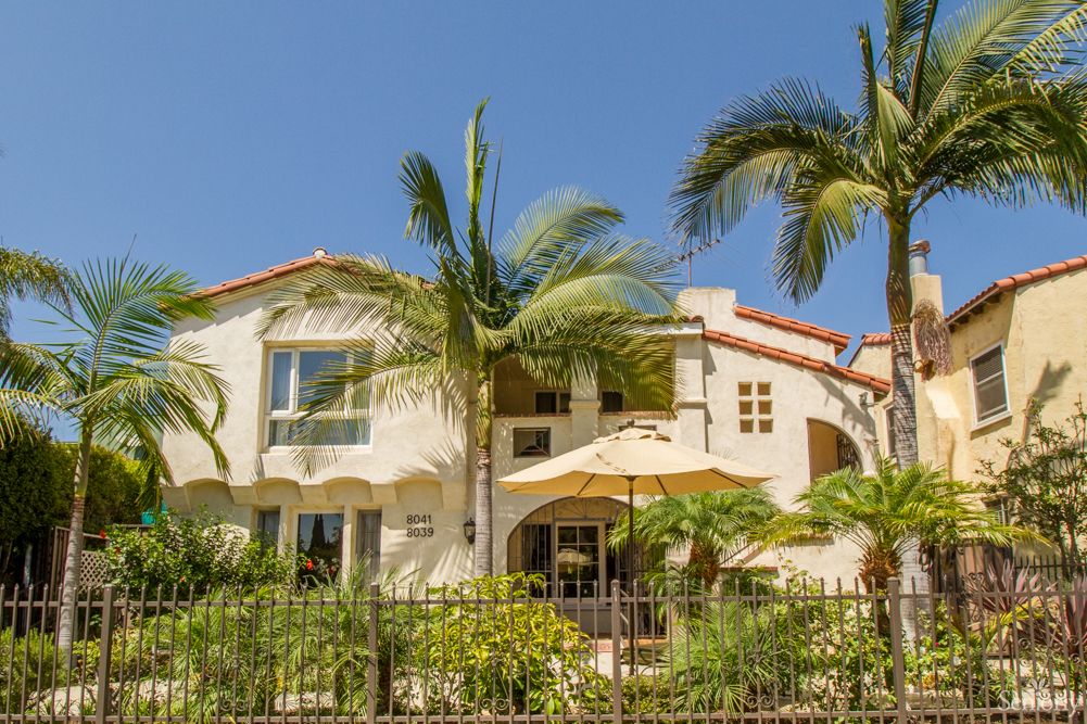 A beautiful tropical-style house surrounded by palm trees and a well-maintained garden on a sunny day.
