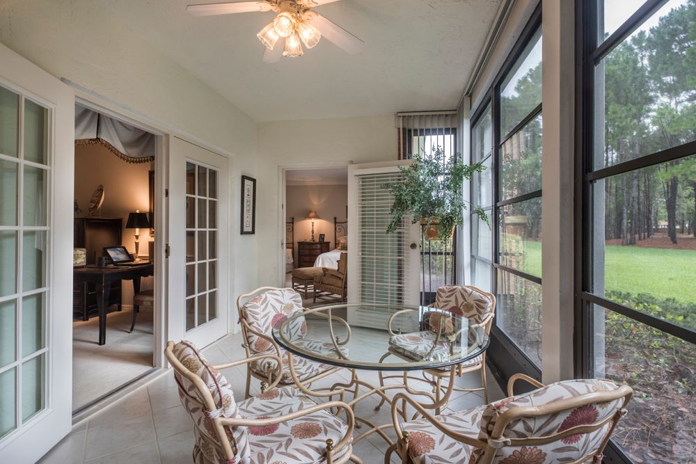A cozy sunroom with a glass table, chairs, and ample natural light streaming through large windows.