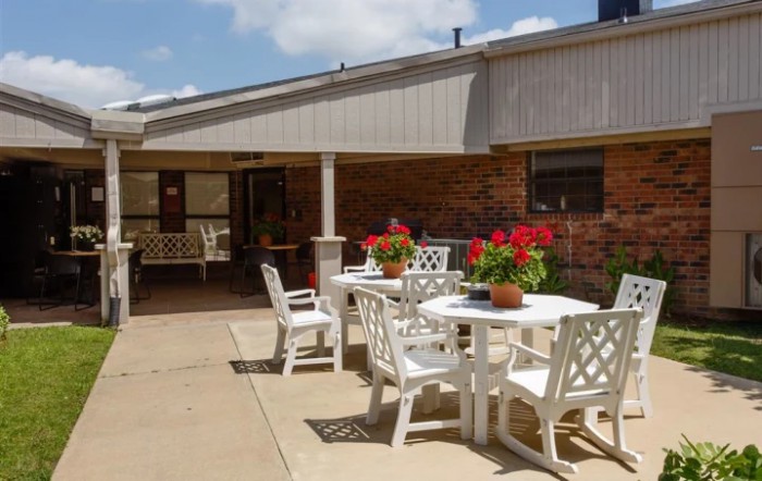 A sunny patio area with white tables and chairs, adorned with potted red flowers.