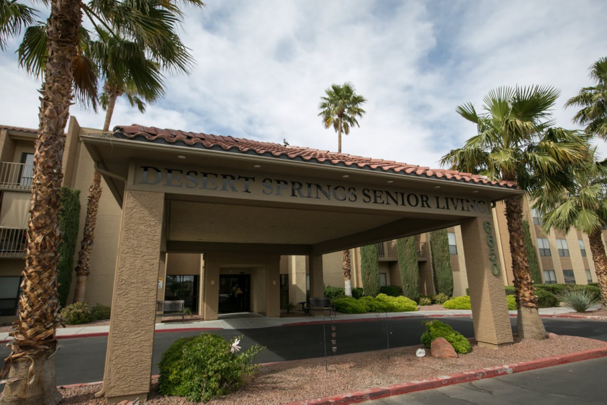 Entrance of a building with palm trees and landscaped surroundings.
