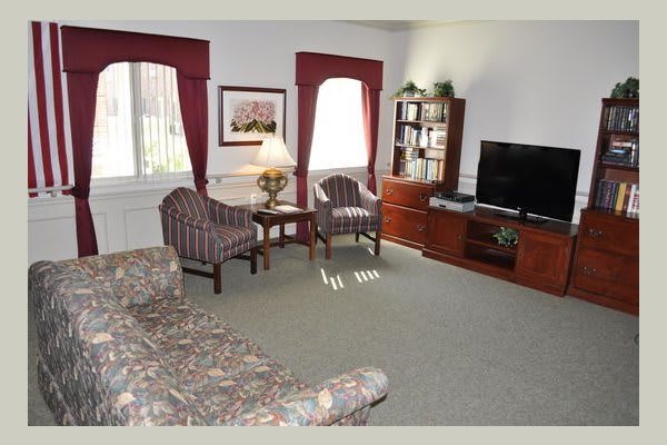 A cozy living room with a sofa, chairs, and a TV, featuring a bookshelf and decorative elements.