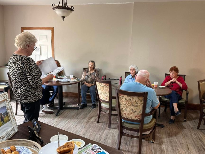 A group of seniors gathered in a room, socializing and having a meeting around tables.