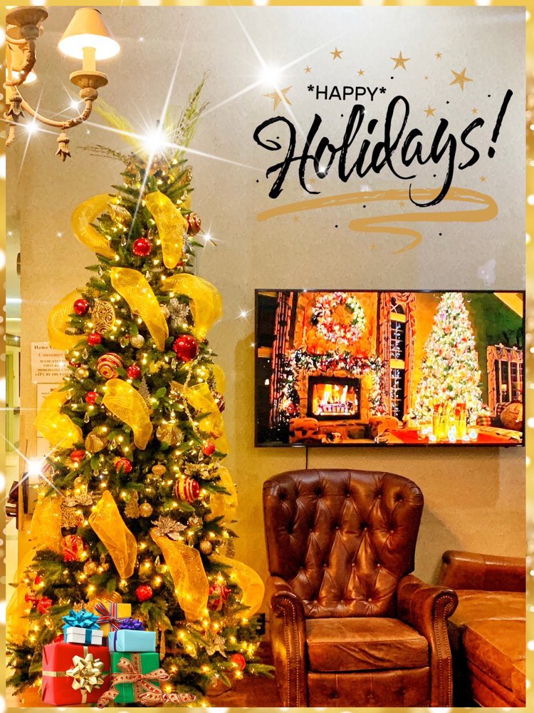 A festive holiday display featuring a beautifully decorated Christmas tree with yellow ribbons and ornaments, accompanied by a cozy chair and an image of a fireplace.
