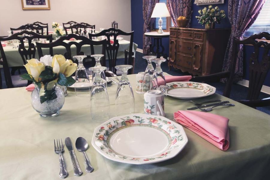 A beautifully set dining table with floral china, cutlery, glassware, and pink napkins in a cozy dining room.