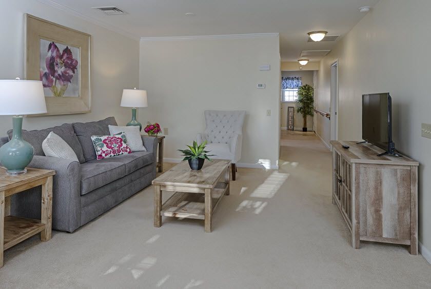 A cozy living room with a sofa, coffee table, and lamp, featuring light decor and carpeted flooring.