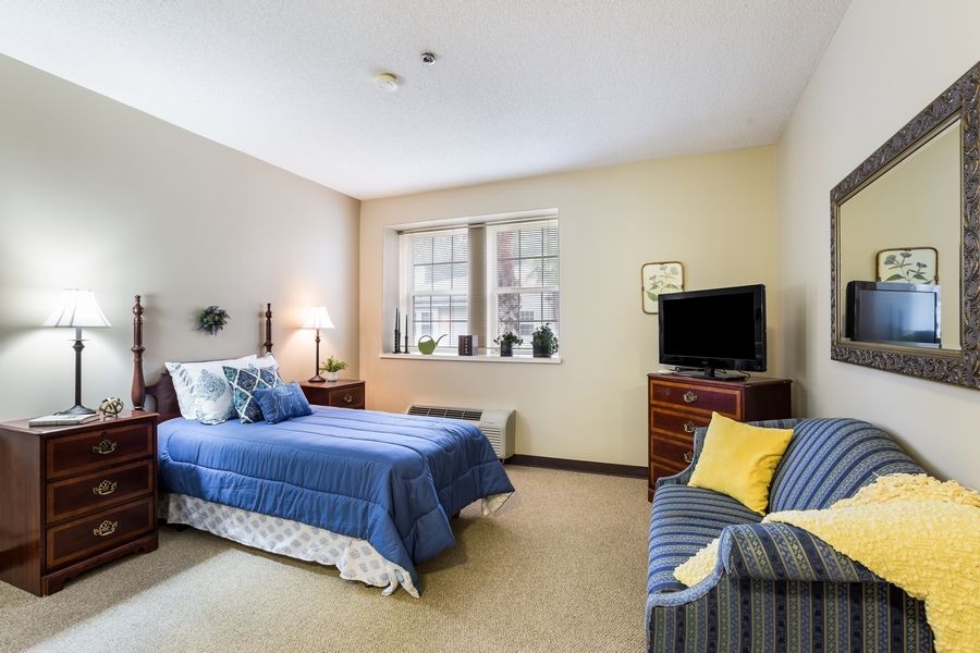 A cozy bedroom with blue bedding, a television, and a window letting in natural light.