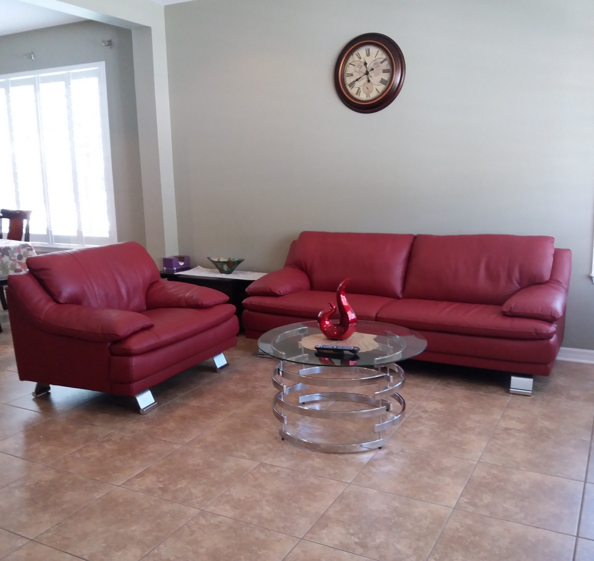 A minimalist living room featuring red sofas, a glass coffee table, and a wall clock.