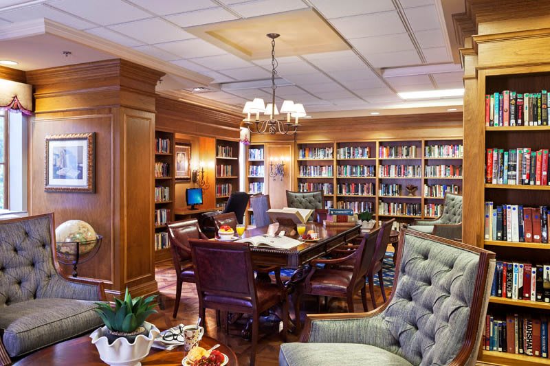 A cozy library room with wooden furniture and bookshelves filled with books, offering comfortable seating and a warm lighting ambiance.