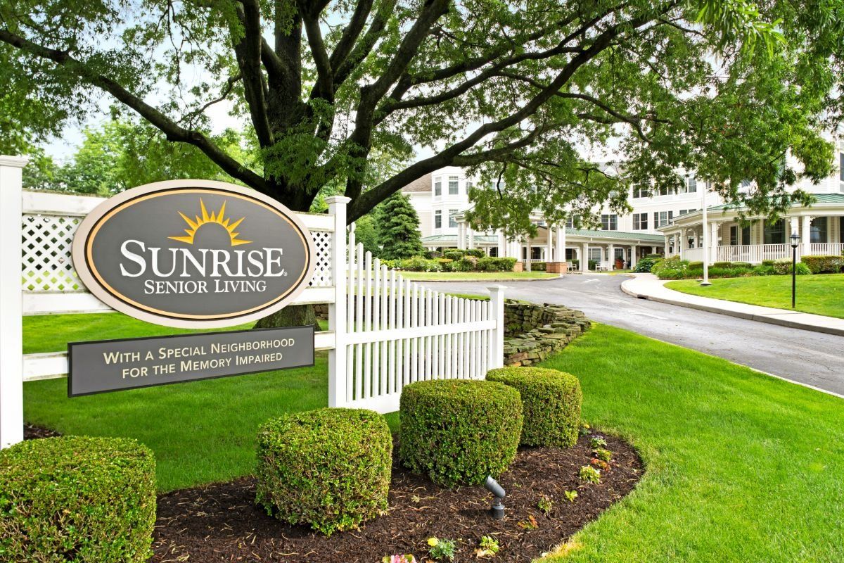 Entrance to a well-maintained retirement community with lush landscaping and a welcoming sign.