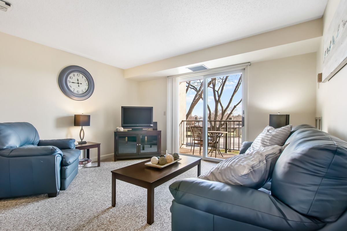 A cozy living room featuring comfortable couches, a television, and a coffee table, with a view of the balcony through glass doors.