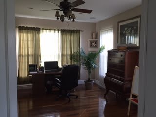 A cozy home office with a desk, computer, and piano by the window.