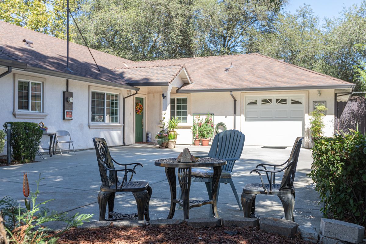 A cozy patio setup outside a single-story house with a garage, surrounded by greenery.