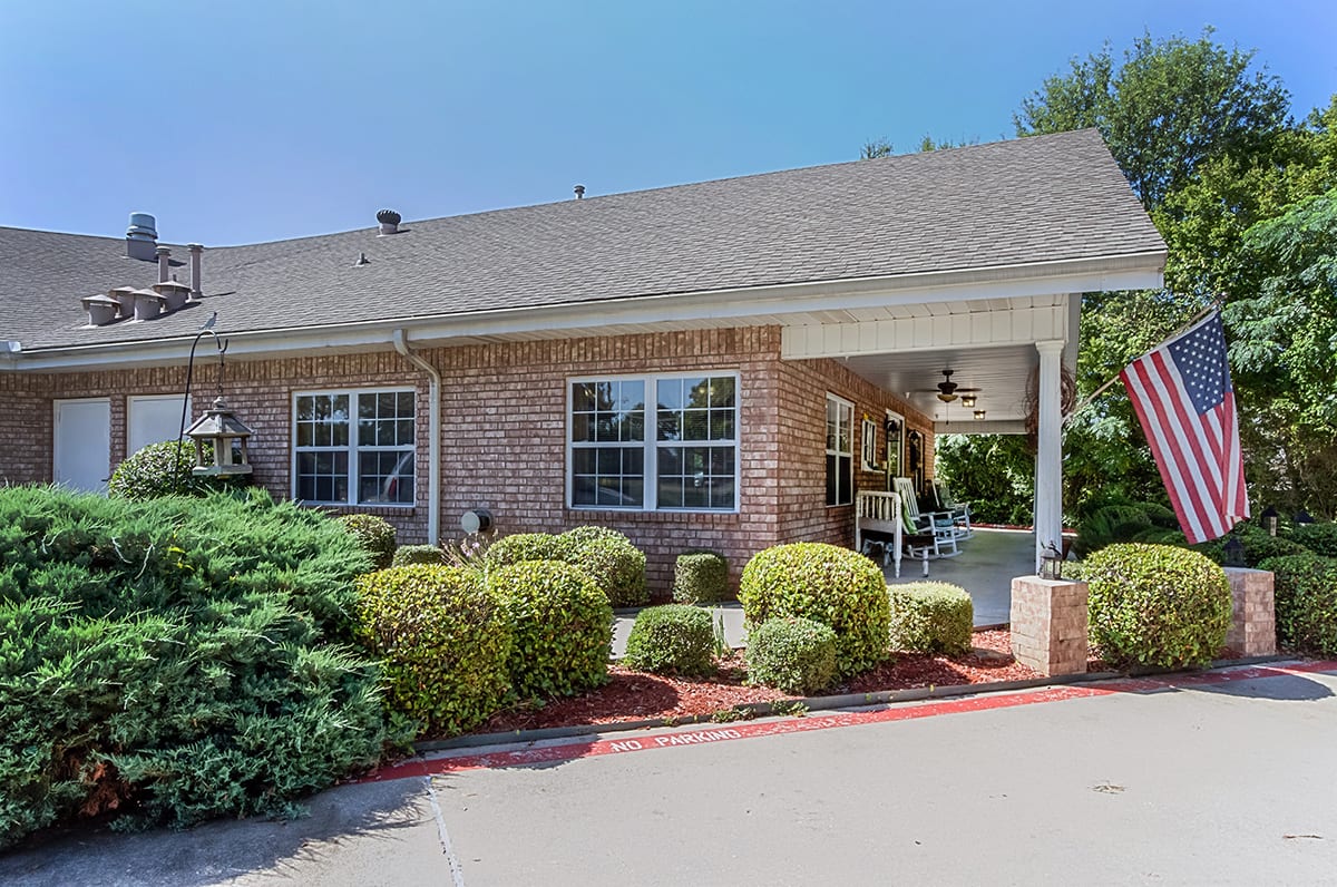 A residential building with a well-maintained landscape featuring bushes and a paved walkway.