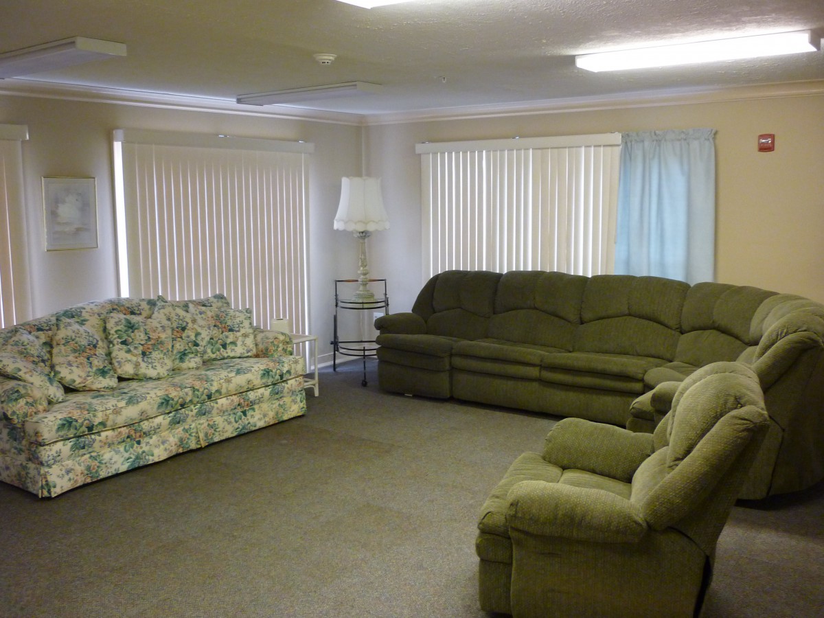 A cozy living room with various sofas and a recliner, featuring vertical blinds and a standing lamp.