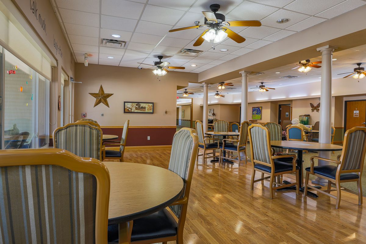 A spacious and well-lit dining area with tables and chairs, featuring ceiling fans and wooden flooring.