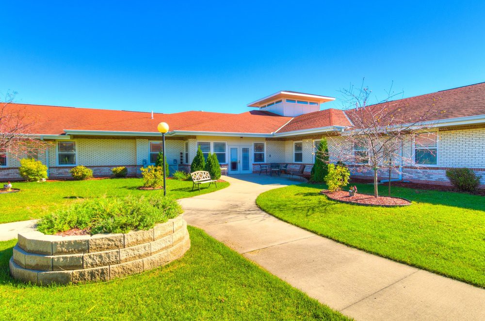 A modern building with a brick exterior, surrounded by a landscaped garden and pathway under a clear blue sky.