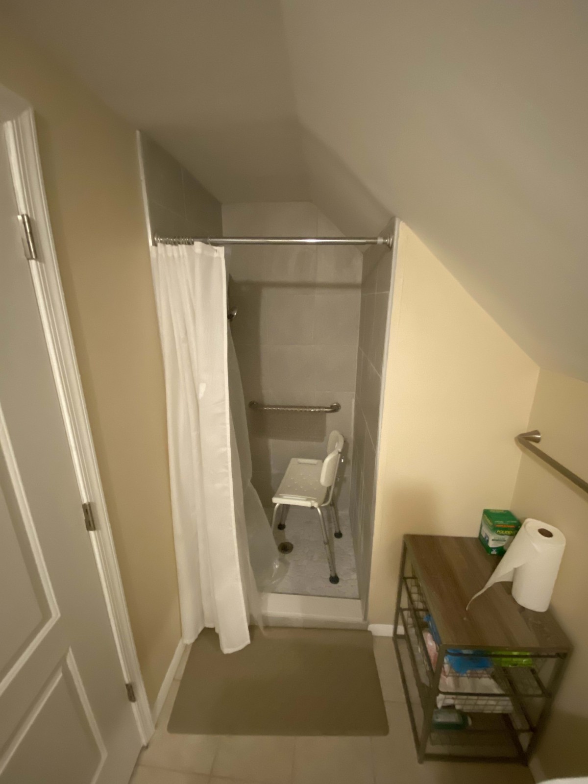 A compact bathroom with a shower area equipped with a chair and curtain.