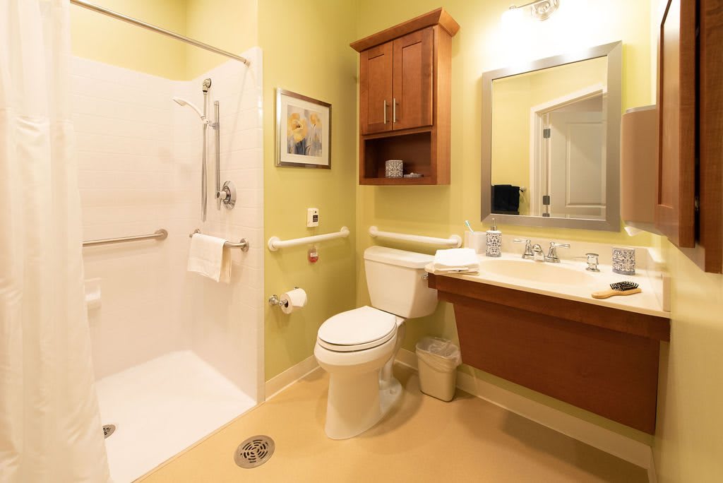 An accessible bathroom with a shower, toilet, and sink equipped with grab bars.