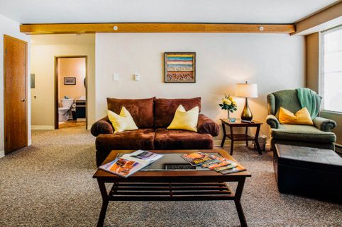 A cozy living room featuring a brown sofa, green armchair, and wooden coffee table with magazines.