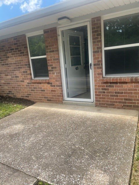A small patio area with a glass door and windows on a brick wall.