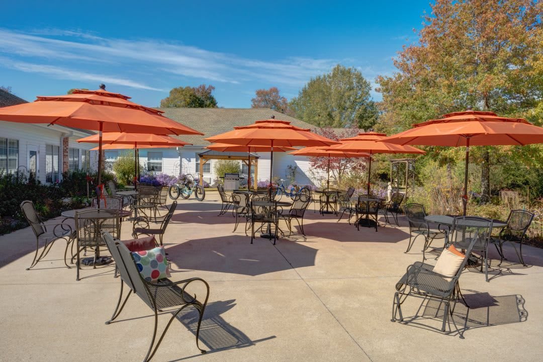A sunny outdoor patio area with tables, chairs, and orange umbrellas.