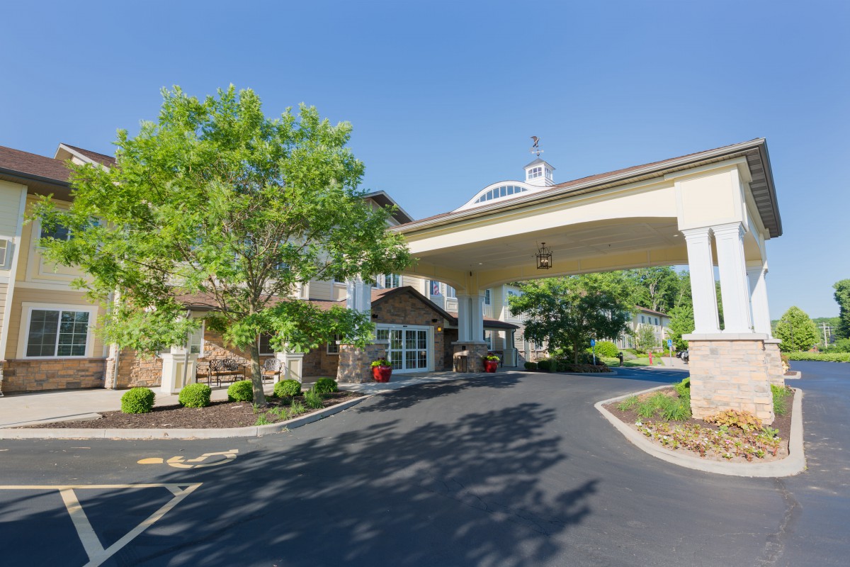 A welcoming hotel entrance with a covered driveway and surrounding greenery under a clear blue sky.