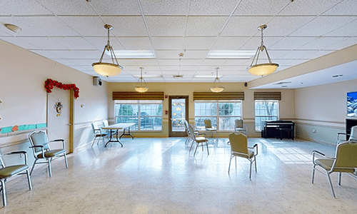 A spacious room with chairs and tables, featuring large windows and overhead lighting.