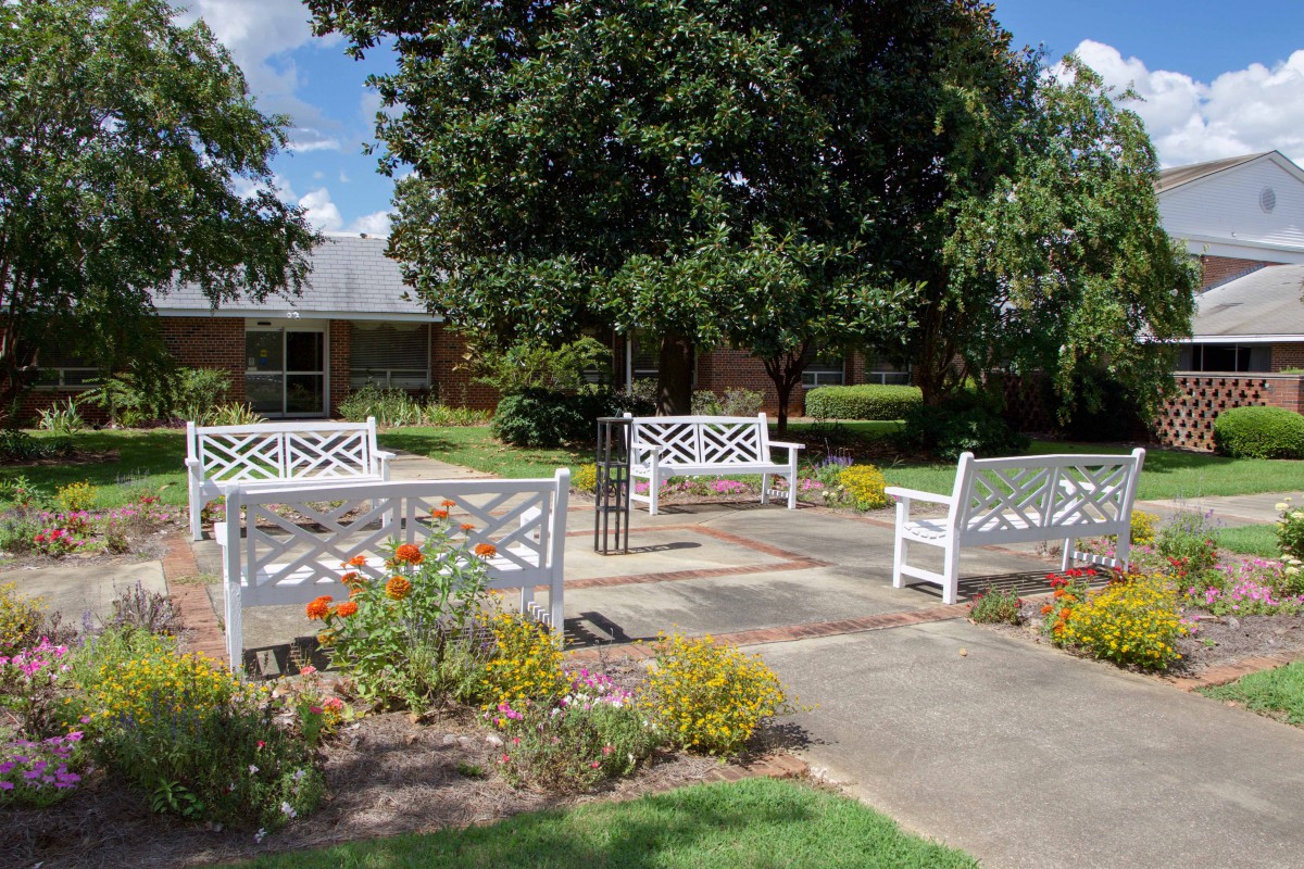 A peaceful garden scene with white benches, colorful flowers, and lush trees.