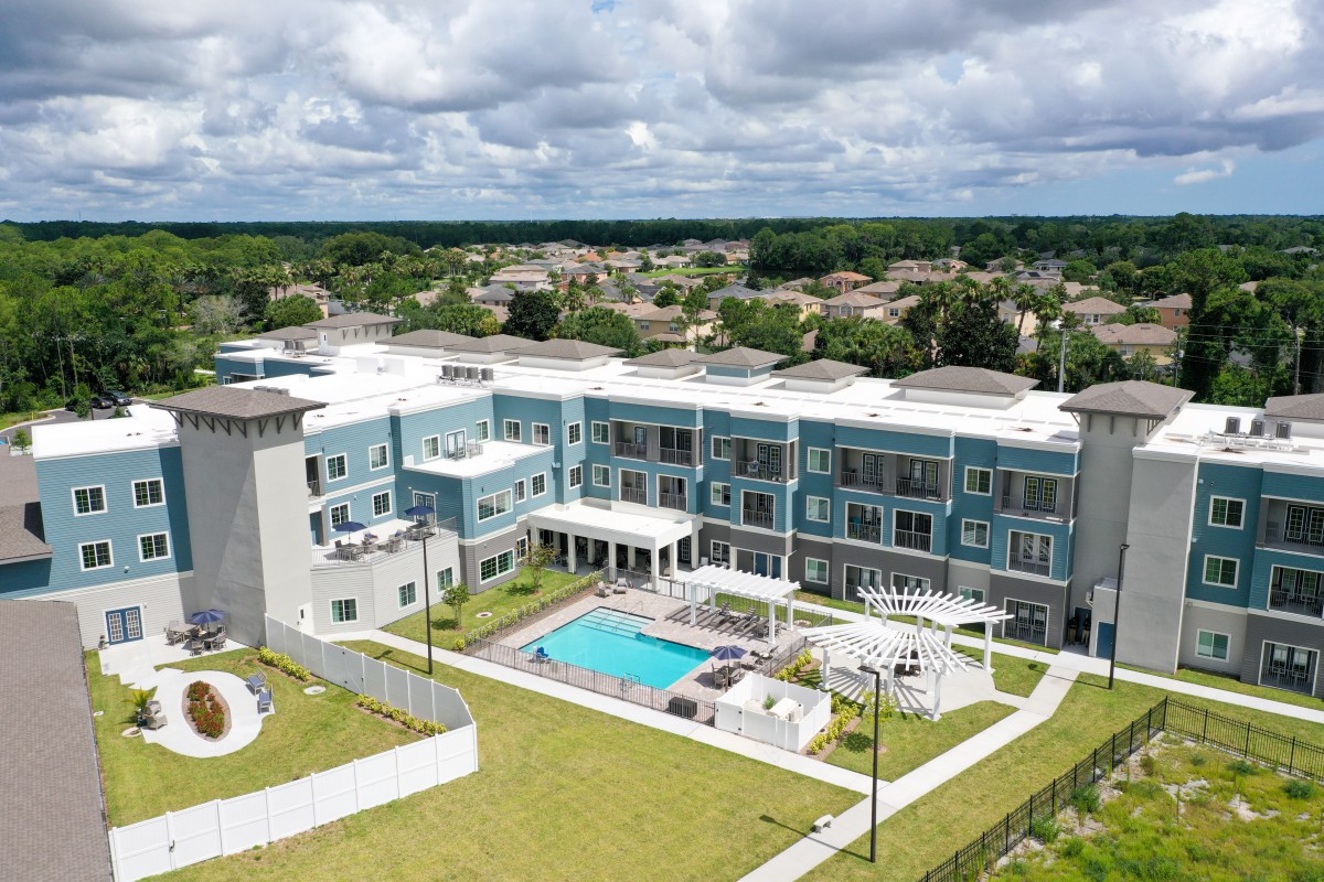 Aerial view of a modern apartment complex featuring a central swimming pool and landscaped surroundings.