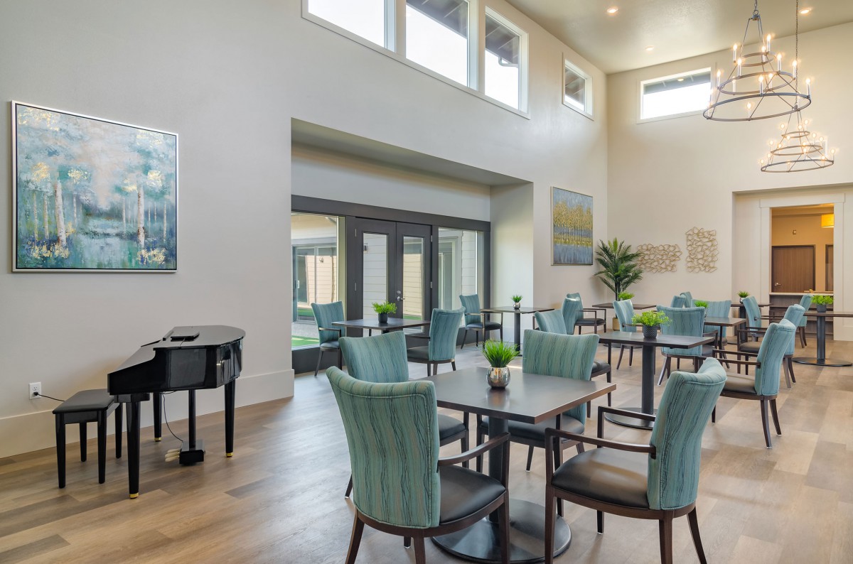 A modern dining area with large windows, stylish chairs and tables, complemented by a grand piano and decorative plants.