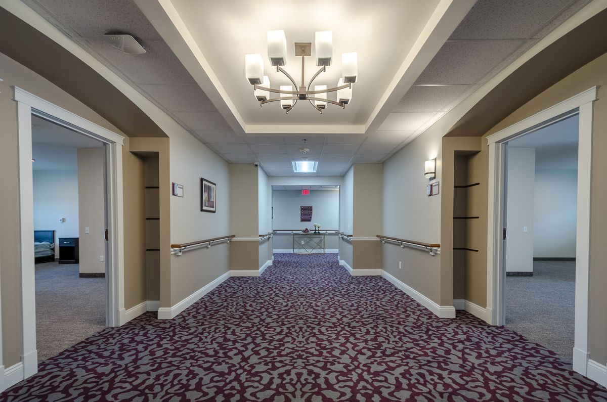 A well-lit hotel hallway with patterned carpet and elegant lighting fixtures.