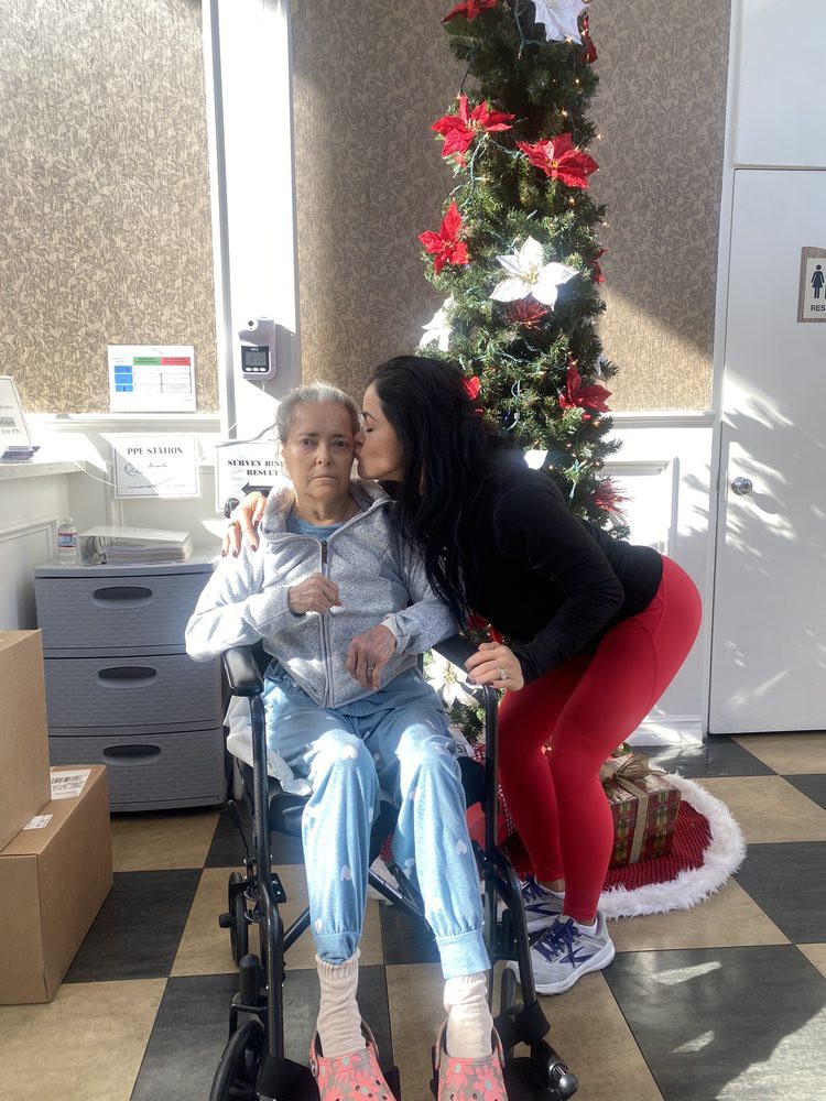 A warm family moment during the Christmas holiday, with an elderly person in a wheelchair receiving a kiss.
