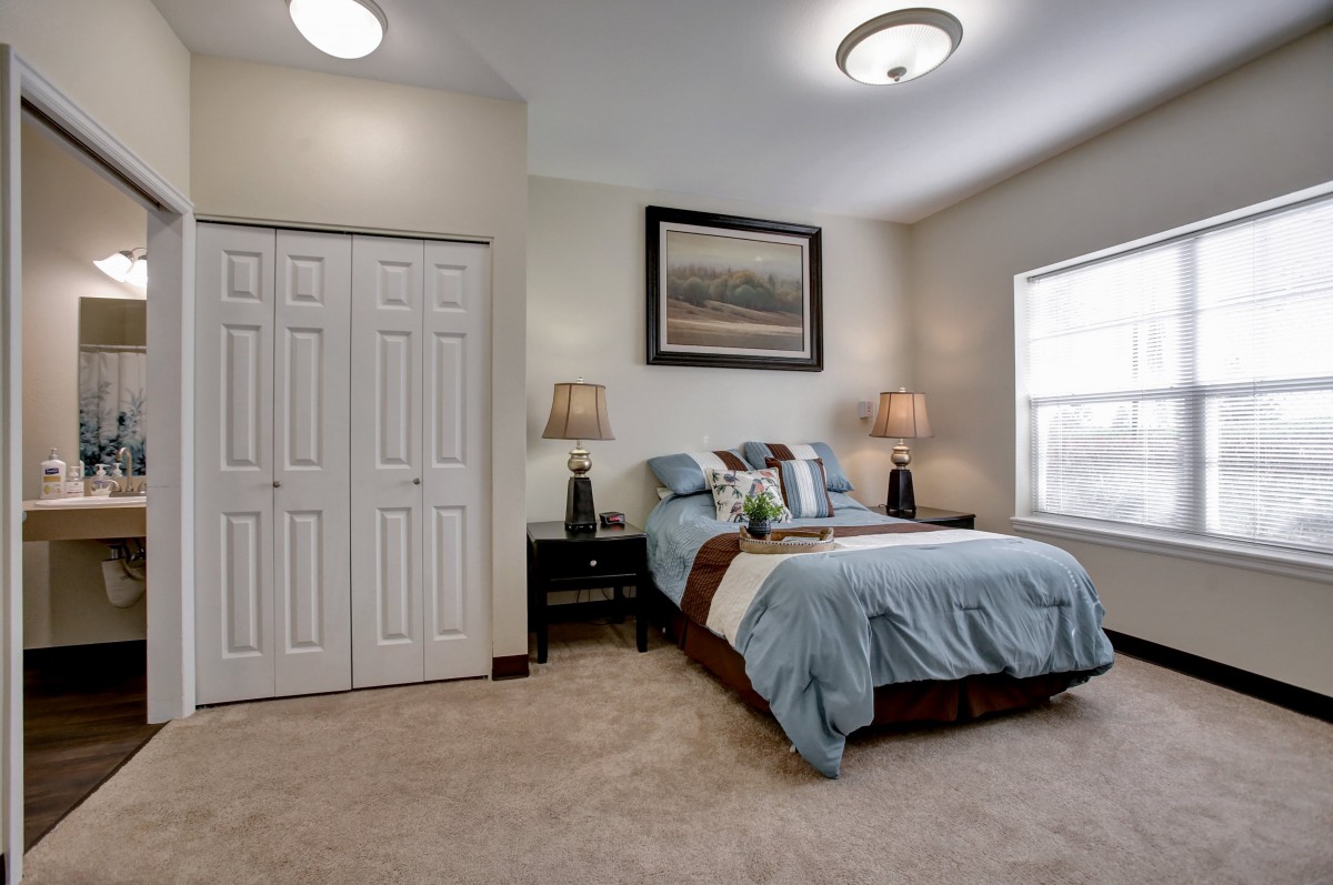 A cozy bedroom with a neatly made bed, two lamps on nightstands, and a framed picture above the headboard.