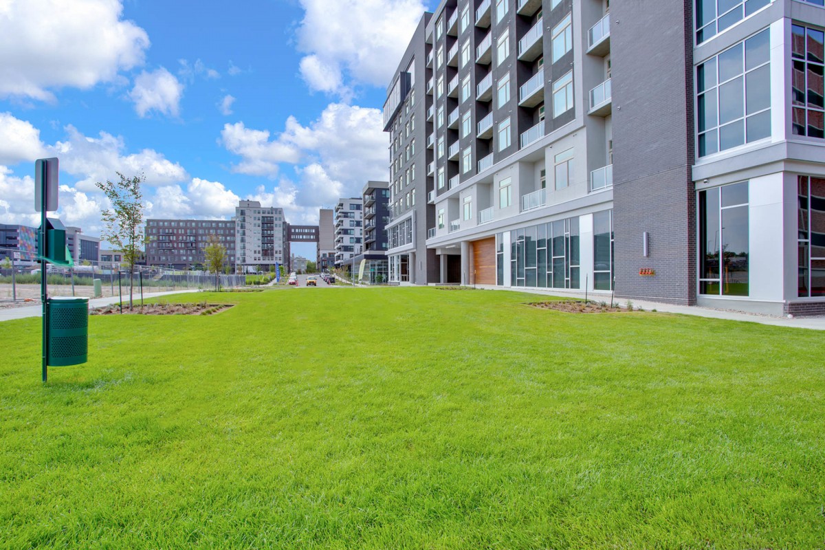 A modern apartment complex with a spacious green lawn under a partly cloudy sky.