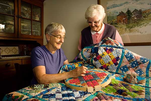 Two elderly women engaged in quilting a colorful patchwork blanket.