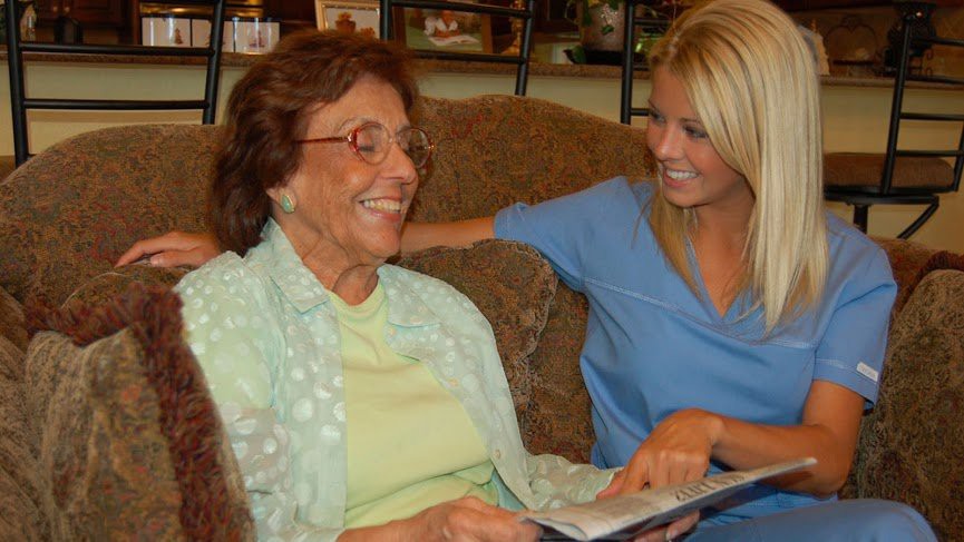 An elderly person and a caregiver sharing a happy moment while looking at a book together.