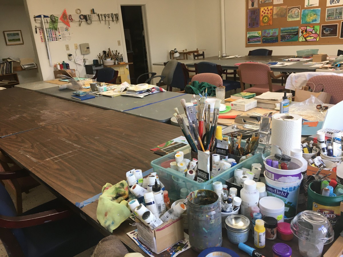 An art studio with tables covered in painting supplies and brushes.