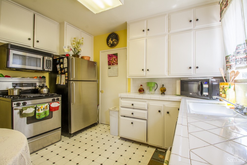 A bright kitchen with white cabinets, stainless steel appliances, and patterned tile flooring.