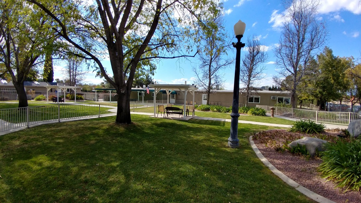 A tranquil park scene with a bench, lamp post, and building under a blue sky.