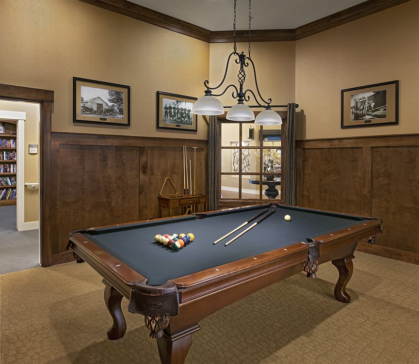 A well-lit billiard room featuring a classic pool table with wooden legs and a hanging chandelier.