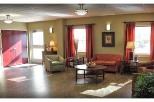 A cozy living room with a sofa, armchair, and coffee table, decorated with red curtains and wall art.