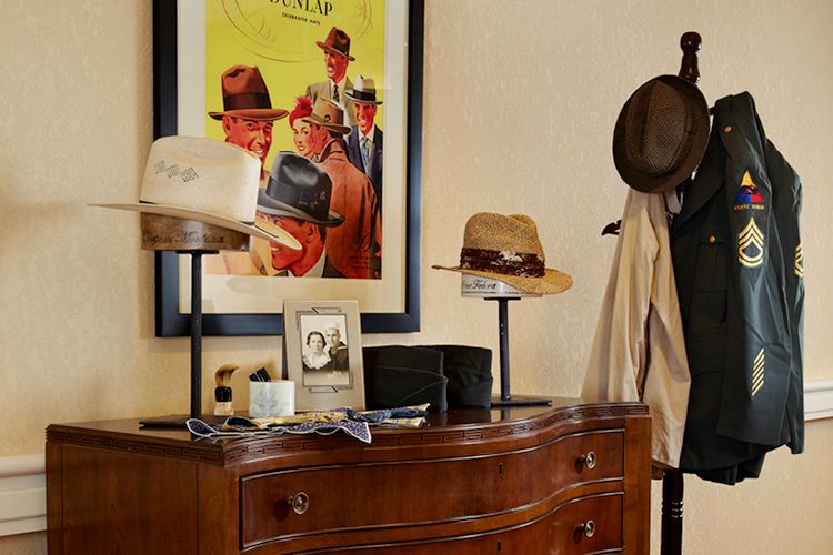 A stylish room featuring a wooden dresser adorned with hats and a framed black-and-white photo, complemented by a vibrant poster and a coat rack.