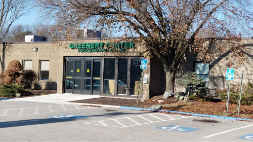 A view of a business establishment featuring large glass windows and signage, surrounded by trees and a parking area.