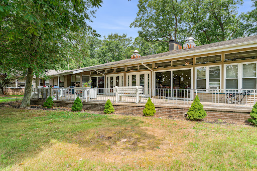 A spacious house surrounded by greenery, featuring a large deck and well-maintained lawn.