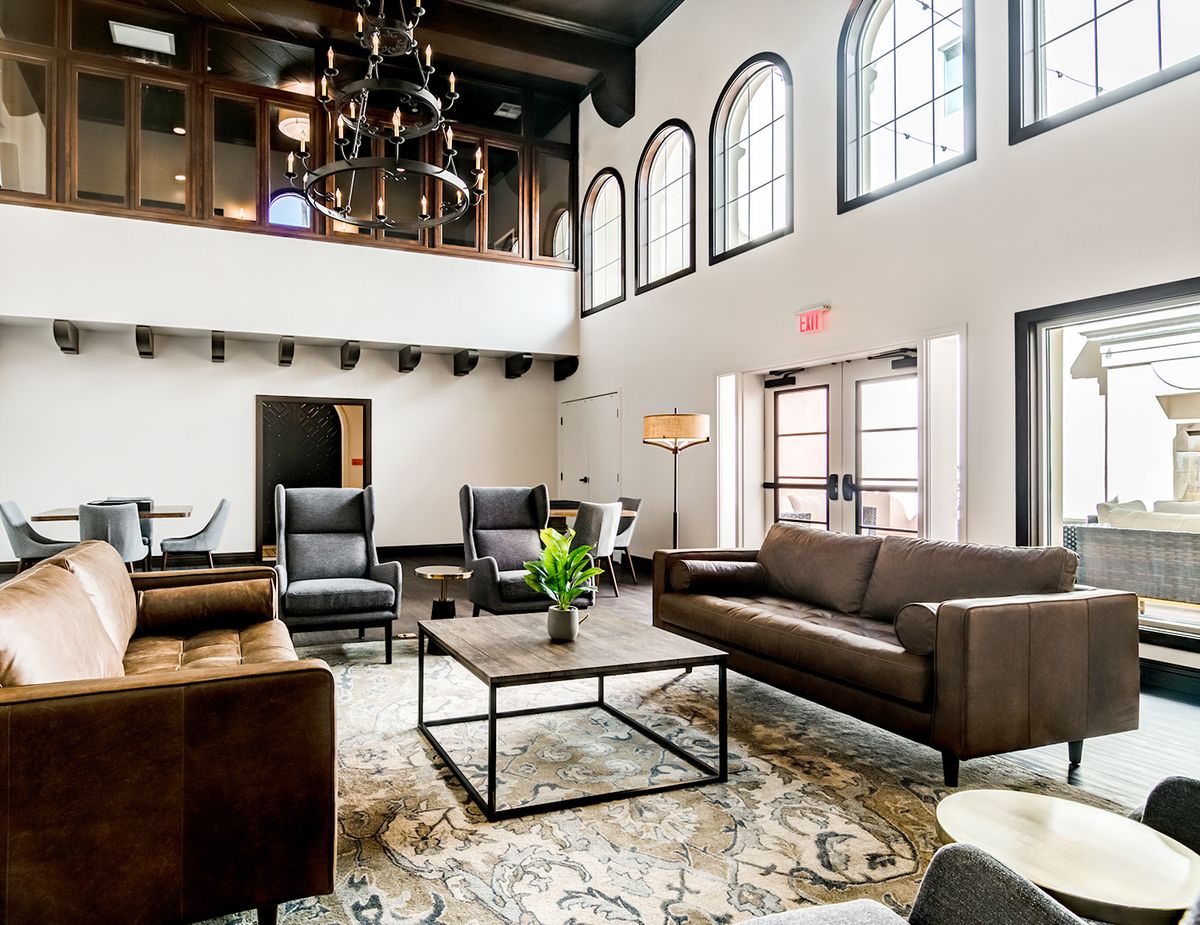 A spacious and elegantly designed living room features modern furniture, a high ceiling, and large arched windows.