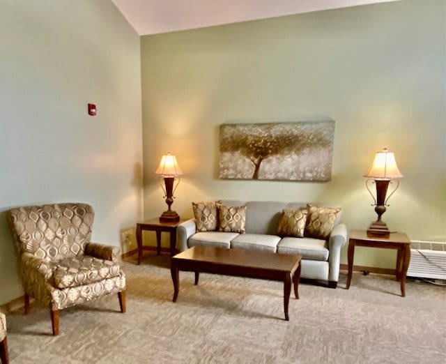 A cozy living room with a sofa, armchair, coffee table, and two lamps flanking a large piece of wall art.